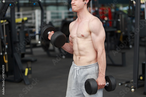 Shirtless young muscular man lift dumbbells in gym. bodybuilder male working out in fitness center.