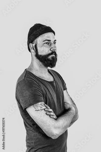 Portrait eines Mannes mit Bart , Mütze auf dem Kopf und Tattoos auf dem Arm in Schwarz/weiß