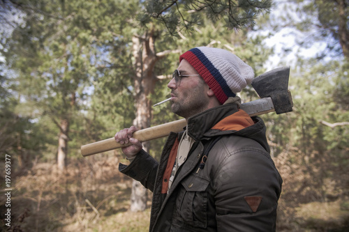 One handsome strong stylish male logger of young man holding wooden axe in forest outdoor and mountains in the background