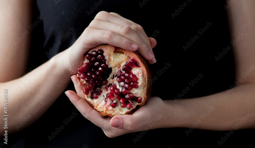Woman hands holding a pomegranate on the black background