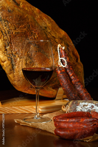 a glass of red wine on a background of Spanish ham jamon in a low key. Drink aperitiv and tapas
