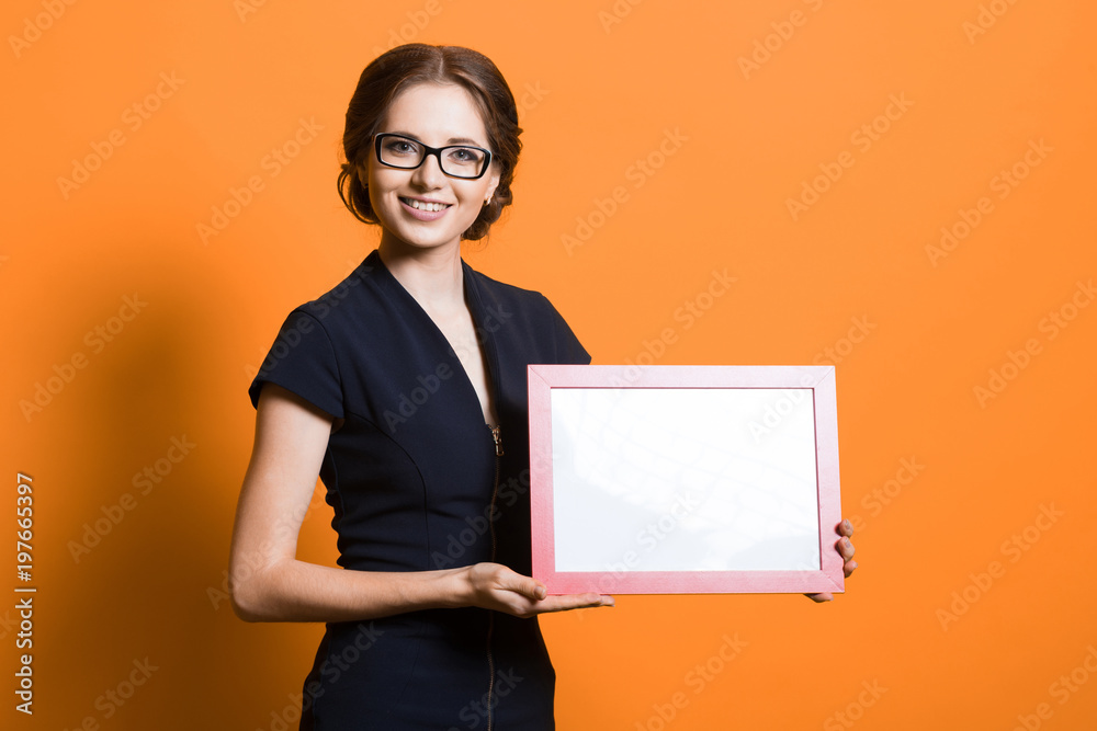 Portrait of confident beautiful young business woman holding frame in her hands standing on orange background