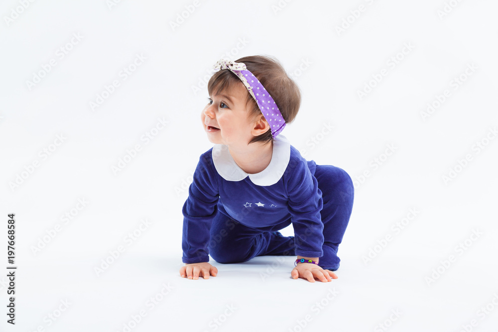 Little cute curious adorable smiling girl with bow in hair crawling sitting in studio posing on white background Little cute curious adorable smiling girl with bow in hair crawling sitting in studio posing on white background
