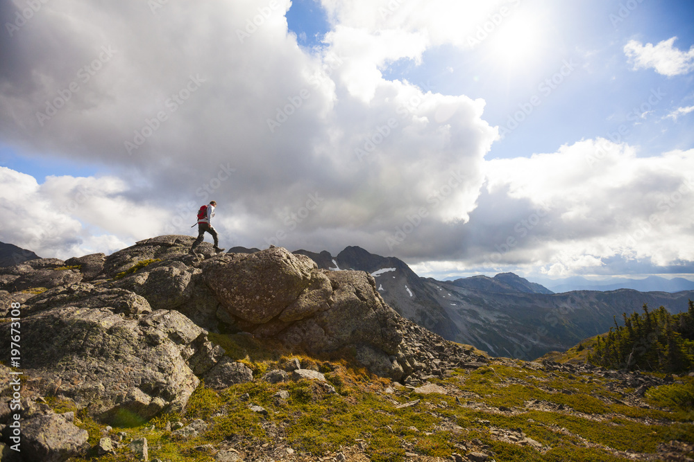 Hiker climbing on rocks against cloudy sky Hiker climbing on rocks against cloudy sky