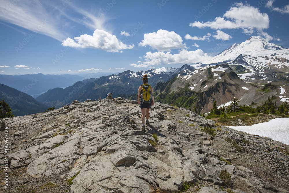 Rear view of female hiker walking on rock formations against mountains and cloudy sky during winter at North Cascades National Park Rear view of female hiker walking on rock formations against mountains and cloudy sky during winter at North Cascades National Park