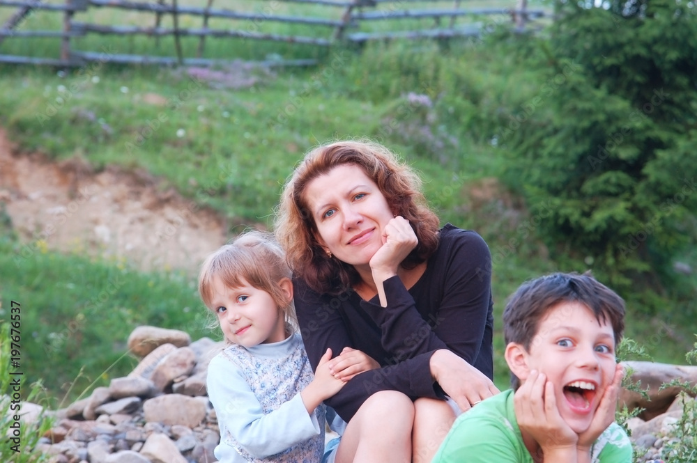 Children with funny faces and a woman, their mom resting on a picnic in the mountains in the summer Children with funny faces and a woman, their mom resting on a picnic in the mountains in the summer