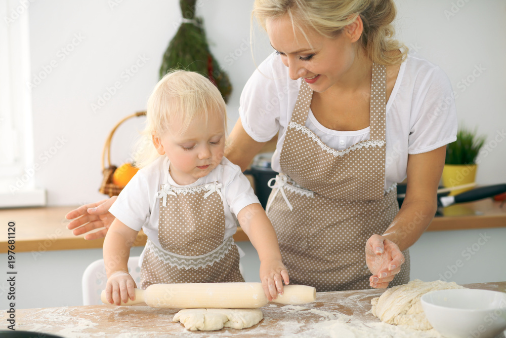 Little girl and her blonde mom in red aprons  playing and laughing while kneading the dough in the kitchen. Homemade pastry for bread, pizza or bake cookies