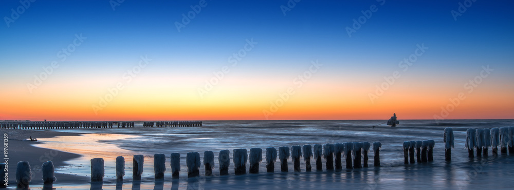 Panorama of a beautiful winter landscape with frozen wooden breakwater at the Baltic Sea. Concept holidays and travel
