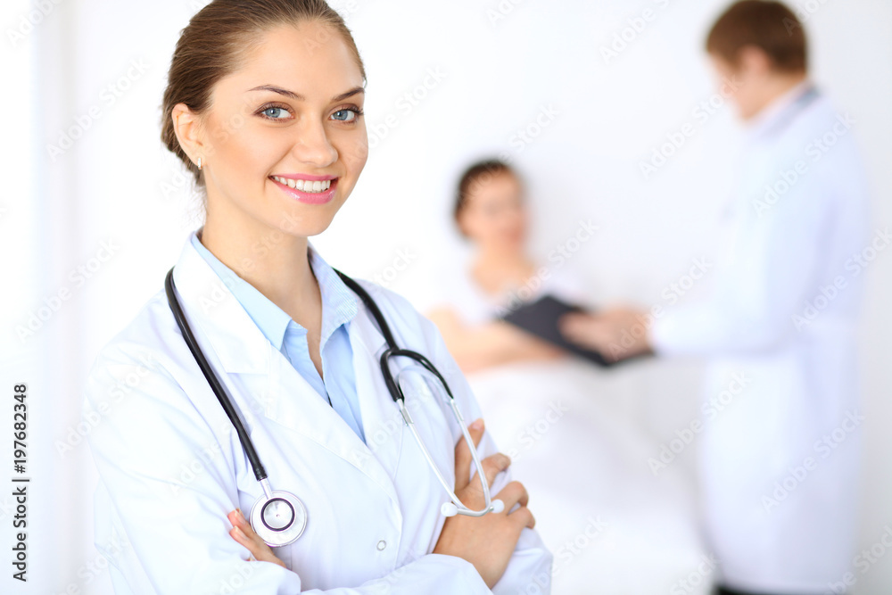 Cheerful smiling female doctor on the background with physician and his patient in the bed Cheerful smiling female doctor on the background with physician and his patient in the bed