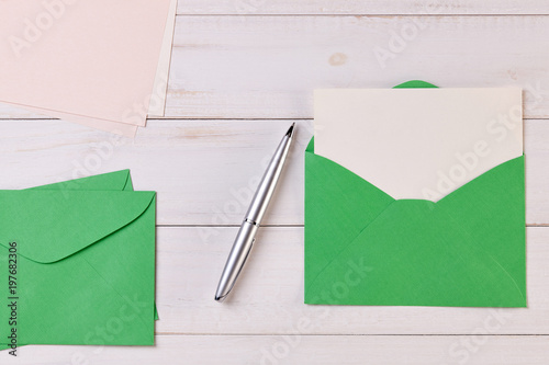 Top View of a invitation or Letter with a Green Envelope. Message or Ticket on Wooden White Desk or Table. Writing a note. Pen, Pencil, a Blank Notebook. Picture. Copy space for text or Image.