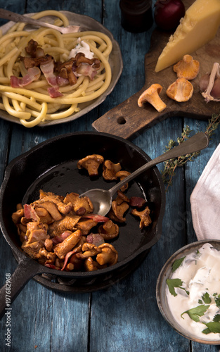 Roasted chanterelles mushrooms on the cast iron pan and spaghetti on rustic wooden table