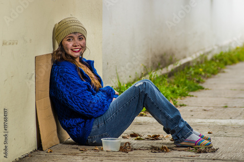 Obraz na plátně Outdoor view of homeless smiling woman begging on the street in cold autumn weat