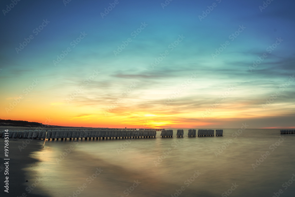 Sunrise, sunset of a beautiful winter landscape with frozen wooden breakwater. Concept holidays and travel