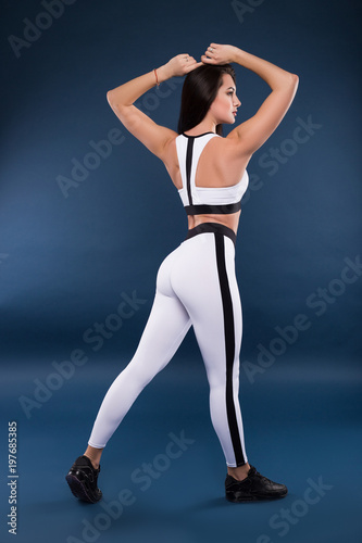 Believe you can and you will! Beautiful sexy fitness woman posing full length for the camera against the dark blue background.