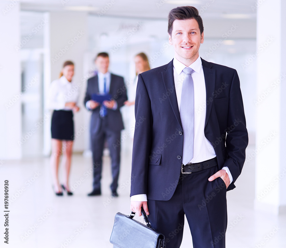 Portrait of young businessman in office with colleagues in the background Portrait of young businessman in office with colleagues in the background