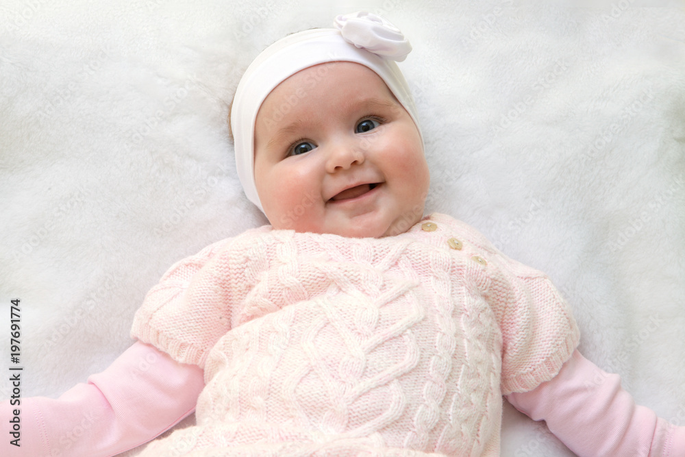 Cute cheerful newborn dressed in pink sweater on white fur blanket. Adorable infant baby with headband. Cute cheerful newborn dressed in pink sweater on white fur blanket. Adorable infant baby with headband.
