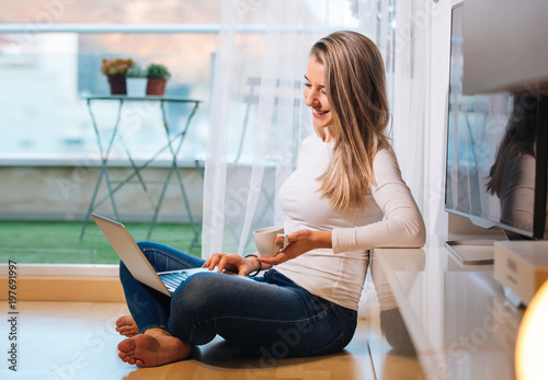 relaxed smiling barefoot woman sitting on the floor looking at her laptop photo