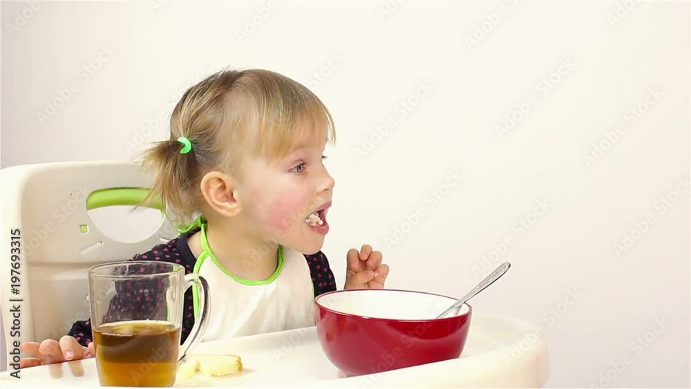 A small two-year-old girl eats porridge. A small two-year-old girl eats porridge.