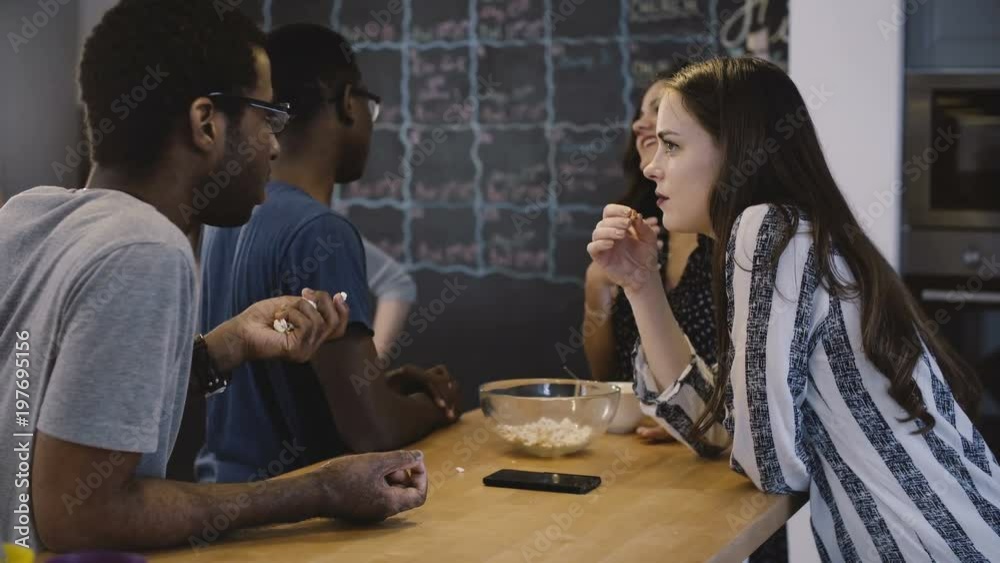 Mixed ethnicity friends chat by a table together. Office open space kitchen. Diverse employees talk and eat snacks. 4K Mixed ethnicity friends chat by a table together. Office open space kitchen. Diverse employees talk and eat snacks. 4K