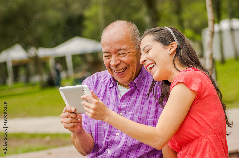 Outdoor view of father and daughter using a tablet looking somethings intefunny, in the park Outdoor view of father and daughter using a tablet looking somethings intefunny, in the park