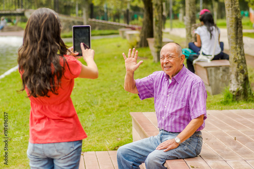 Outdoor view of daughter taking pictures with a tablet to his father in the park