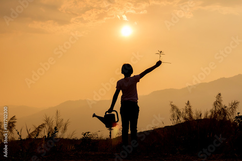 Happy little girl holding plants at sunset background