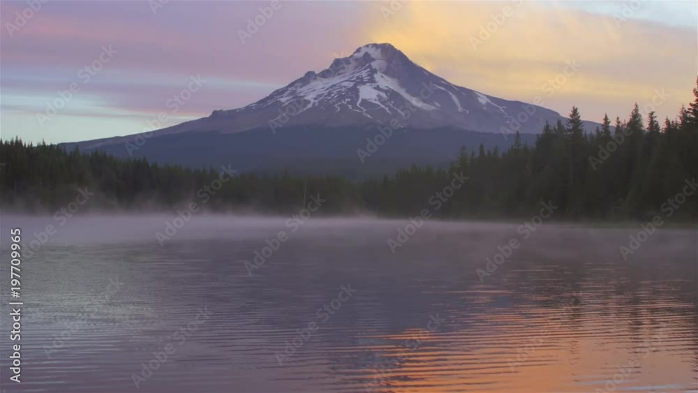 Scenic shot of a lake with morning fog, and a mountain in the background at sunrise