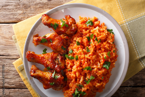 Porcion of African Jollof rice with fried chicken wings close-up on a plate. Horizontal top view