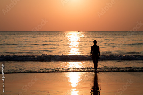Silhouette of the young woman standing in the water during golden sunset. A girl is ready to enter to the sea at sunset in Thailand