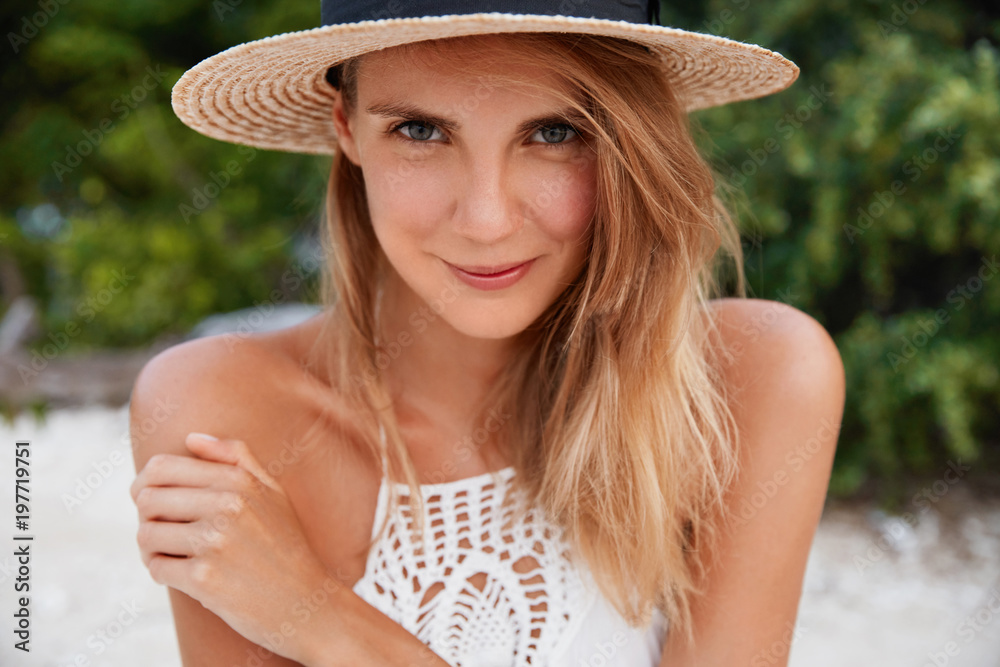 Fotografija Close up shot of pleasant looking with long hair, has pure healthy skin, wears straw hat, poses outdoor, recreats in paradise place with lover, has pleased expression