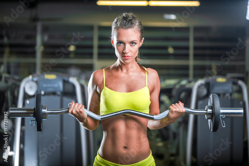 Young tired strong skinny sporty athletic sportswoman woman in sportswear training biceps by barbell in a gym Workout sport motivation ...