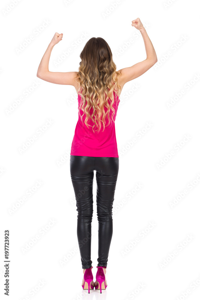 Woman In Leather Trousers And Pink Top Is Flexing Muscles. Rear View. Woman In Leather Trousers And Pink Top Is Flexing Muscles. Rear View.