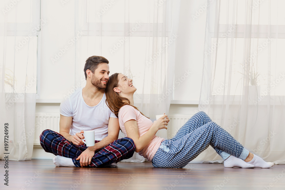 Fototapeta premium A loving couple laughs on the floor against the window in the room.