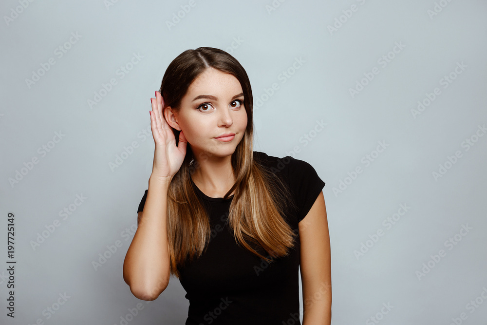 Positive emotions and feelings on white background.Caucasian female with long hair, wearing black T-shirt, holding hand behind ear like she doesnt hear what she is told to do Positive emotions and feelings on white background.Caucasian female with long hair, wearing black T-shirt, holding hand behind ear like she doesnt hear what she is told to do