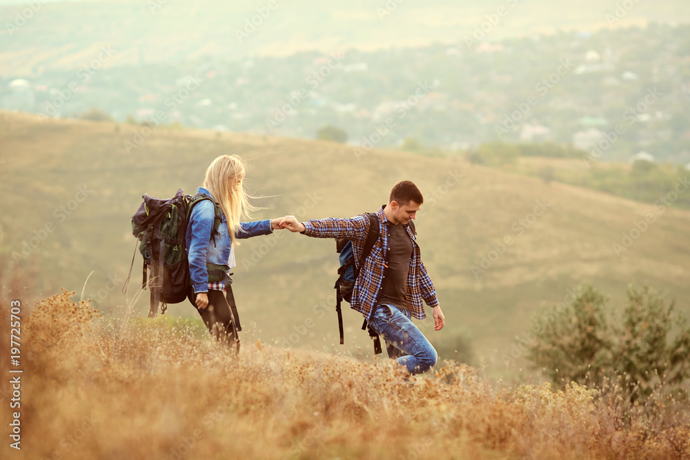 A young couple of tourists with backpacks are walking in nature.