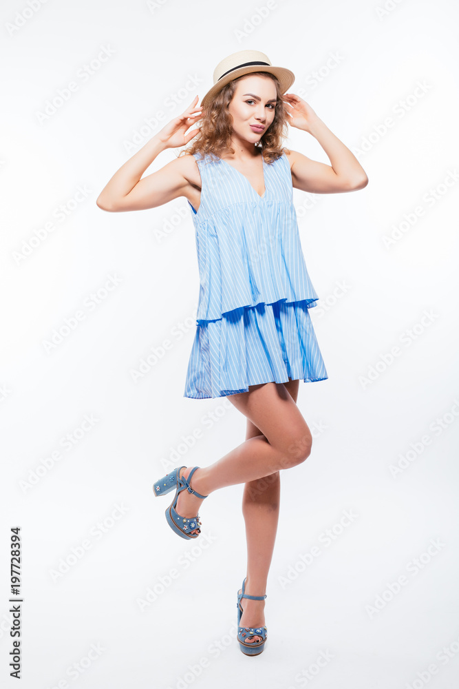 Naklejka premium Full length portrait of a cheerful pretty woman in summer dress and hat posing while standing and looking away at copy space isolated over white background