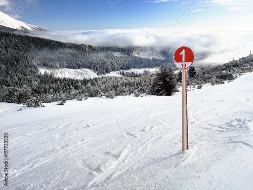 Red ski route 1 sign on fresh snow with snow covered forest and sky in background. Strbske pleso ski resort, Slovakia