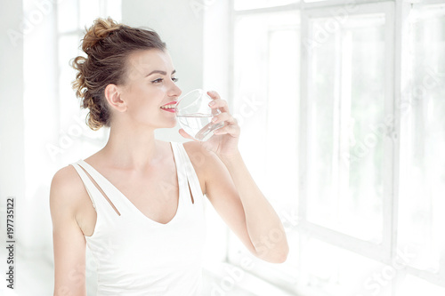 Portrait of a beautiful young woman with a healthy lifestyle smiling while drinking a glass of plain water indoors