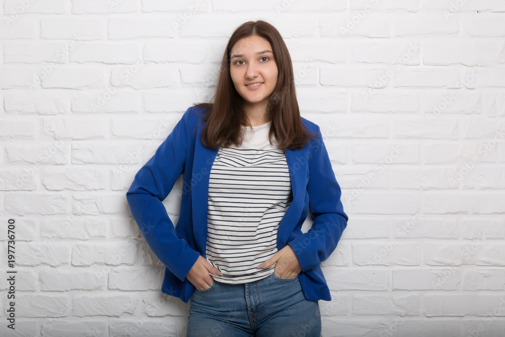 A young pretty smiling girl against a white loft-style brick wall. She looks at the viewer. Copy space. A young pretty smiling girl against a white loft-style brick wall. She looks at the viewer. Copy space.