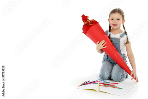Hübsches kleines Mädchen mit einer Schultüte kniet auf weissem Untergrund Malstifte auf dem Boden