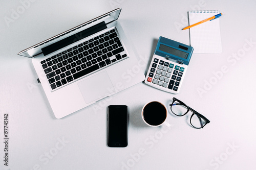 Work space table with laptop, phone, calculator, eyeglasses and coffee on grey background. Top view, Flat lay