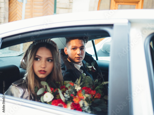 Groom and bride with bouquet of flowers in the wedding car