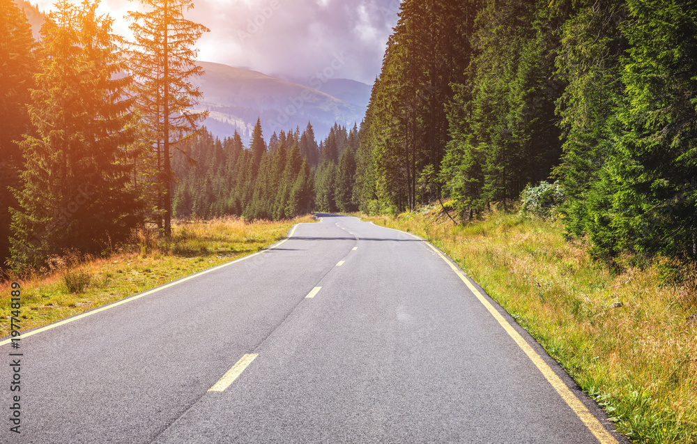 Obraz premium Mountain road. Landscape with rocks, sunny sky with clouds and beautiful asphalt road in the evening in summer. Vintage toning. Travel background. Highway in mountains. Transportation