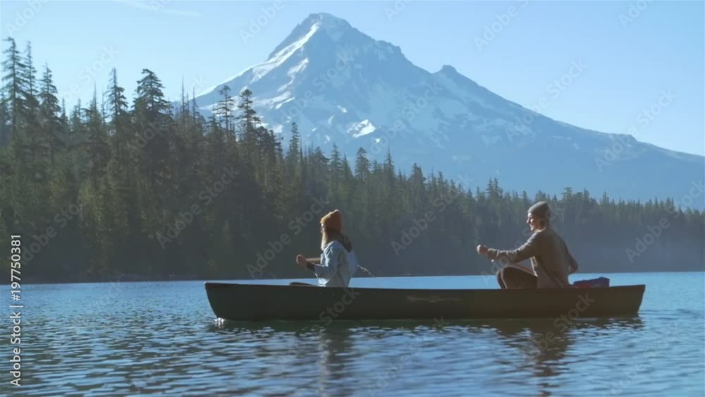 Wide shot of a young loving couple rowing a boat together with some paddles on a lake