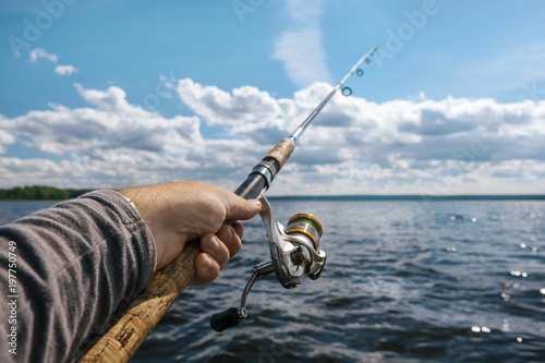 fishing rod in the hand on the background of a wide river on a s