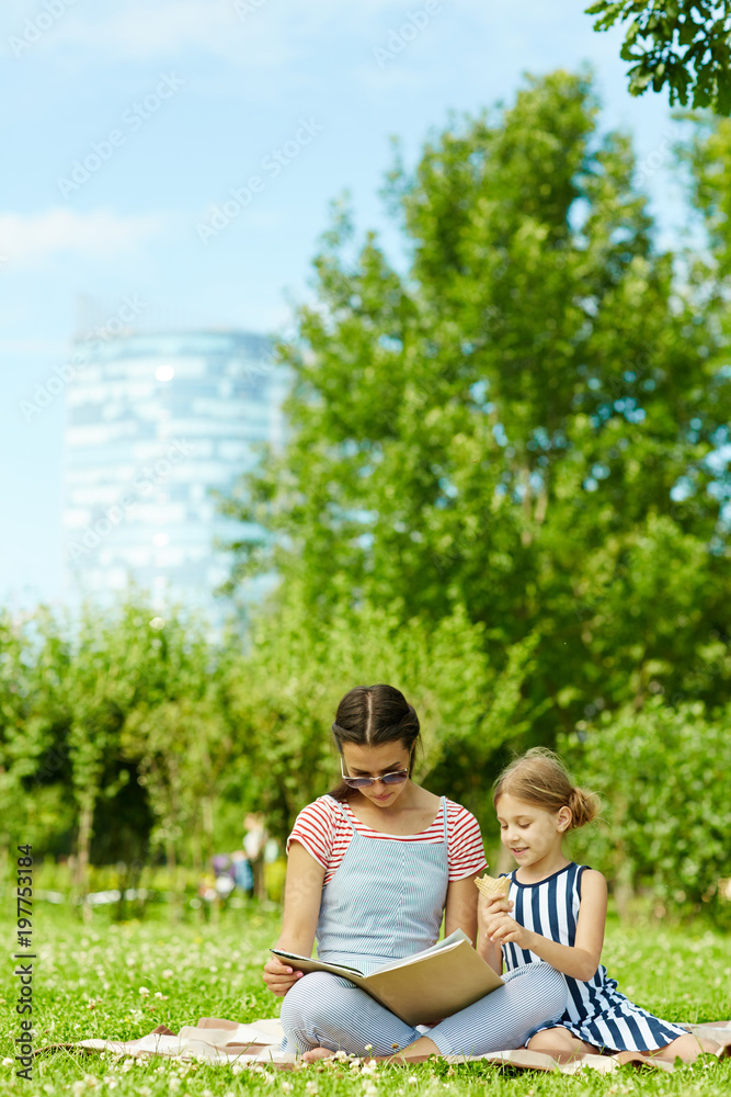 Young woman and little girl reading tales while spending summer day in park Young woman and little girl reading tales while spending summer day in park