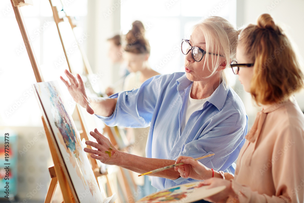 Fototapeta premium Experienced teacher consulting one of students about her painting during lesson in arts school
