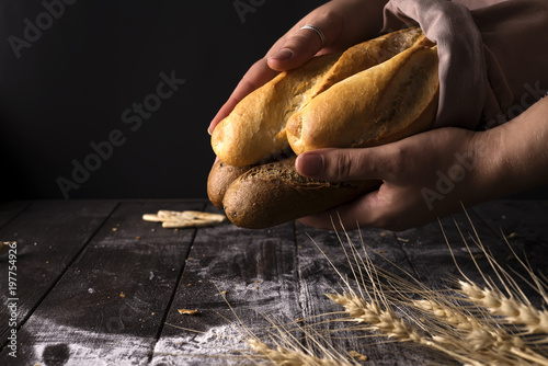 Baker woman holding rustic organic loaf of bread in hands - rural bakery. Natural light  moody still life.