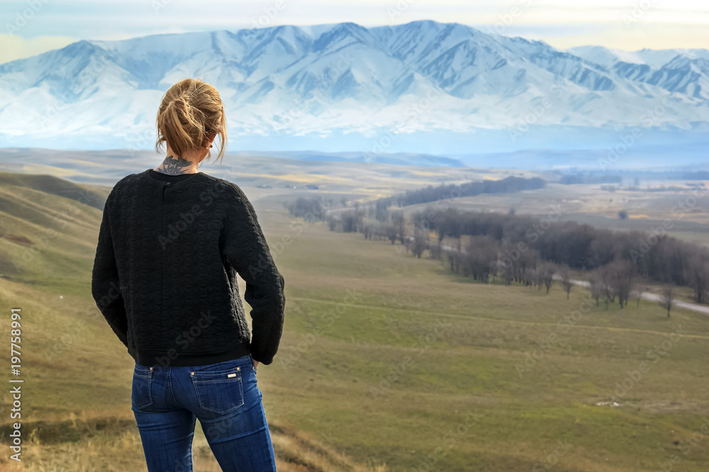 young woman stands and looks at the snow-capped mountains