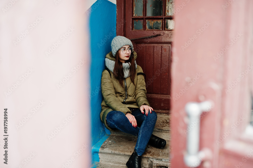 Portrait of brunette girl in gray scarf and hat, glasses against entrance. Portrait of brunette girl in gray scarf and hat, glasses against entrance.